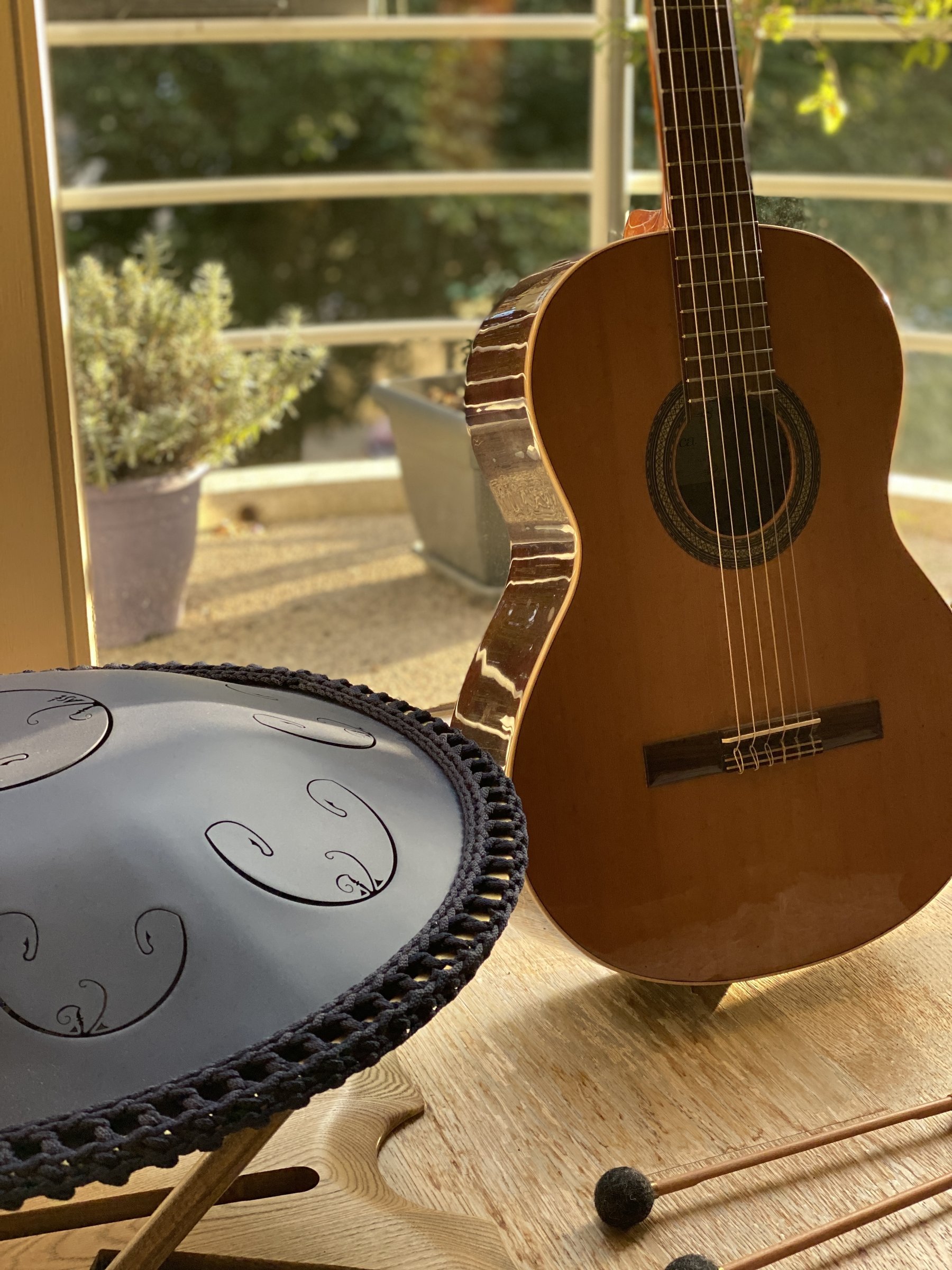 A guitar and a handpan waiting on a table by a window