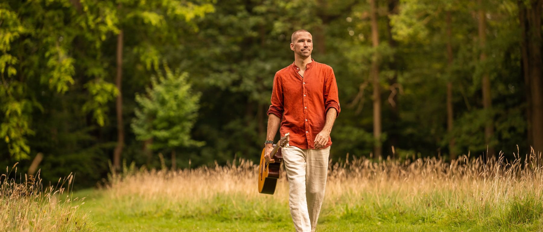 Jorn Ayan walking through a forest with a guitar