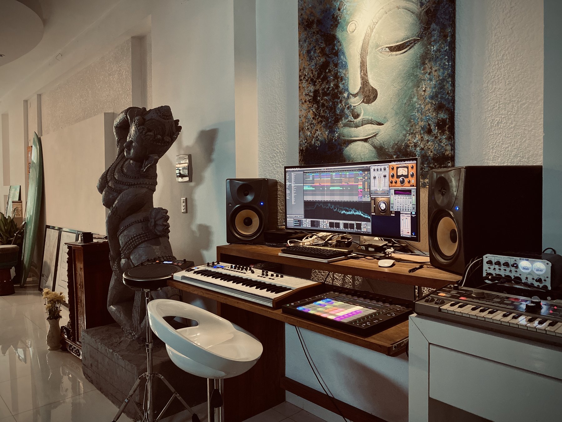 Jorn Ayan's home recording studio, with monitors, MIDI keyboards and a painting of a serene face on the wall