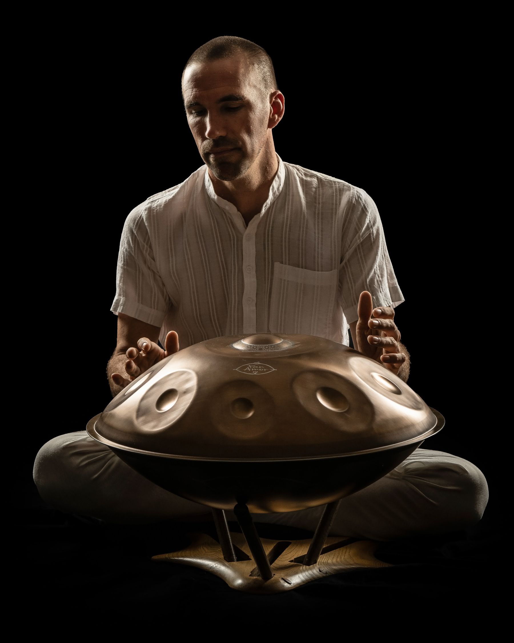 Jorn Ayan playing a handpan, lit against black
