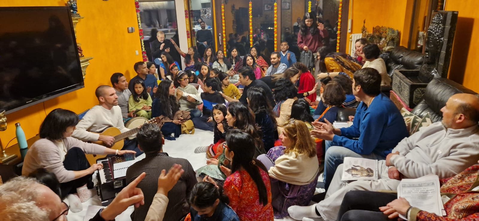 A living-room HeartString gathering, guests seated on cushions and chairs around the musician
