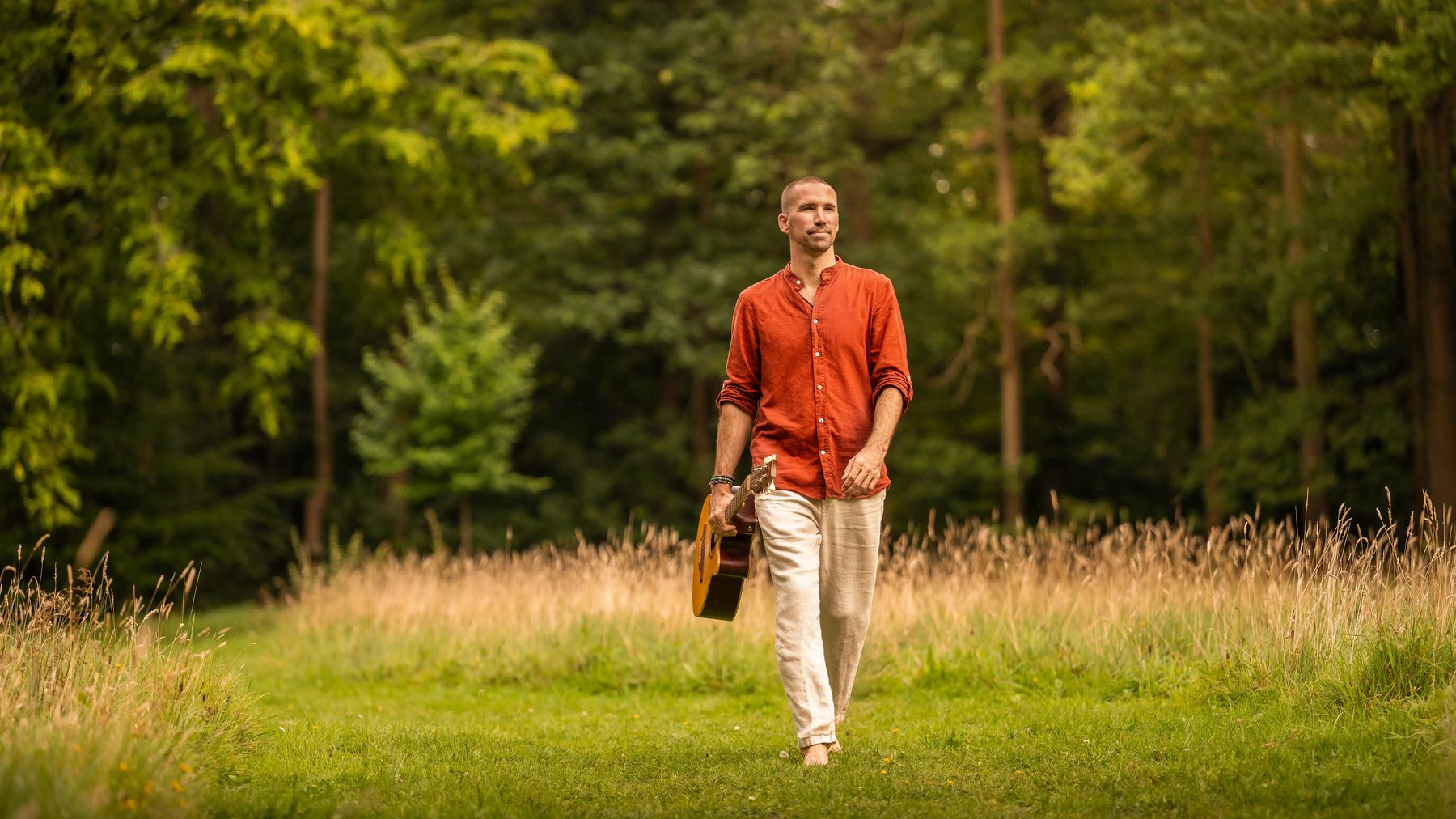 Jorn Ayan walking through a forest clearing carrying a guitar
